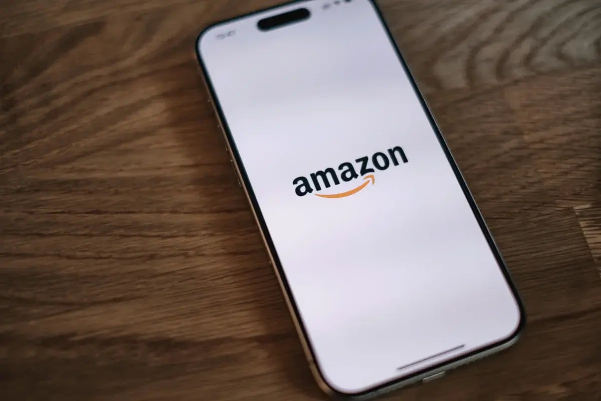 Smartphone on a wooden table displaying the Amazon logo on the screen. The image conveys technology and online shopping with a minimalist tone.