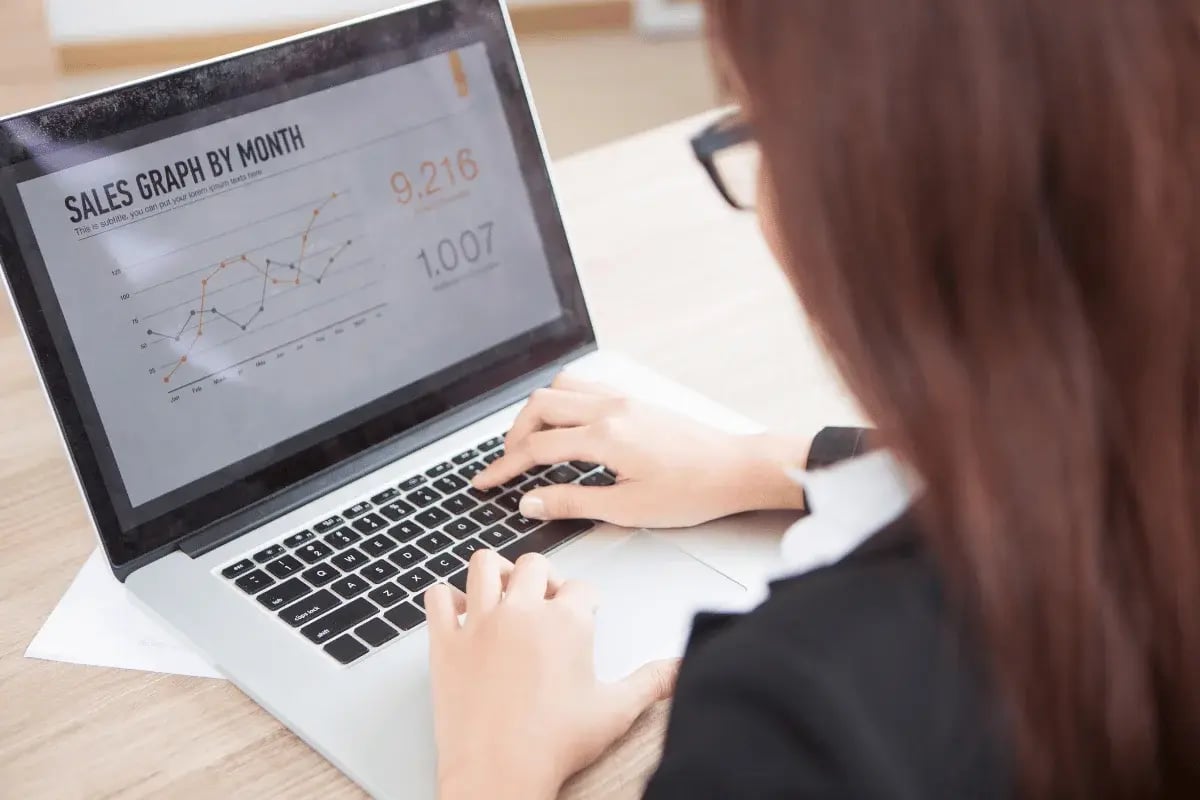 A person in a suit types on a laptop displaying a sales graph by month, highlighting data points for analysis.