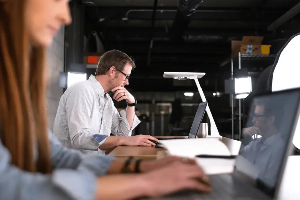 Coworkers seated around a table with laptops in a collaborative office setting.